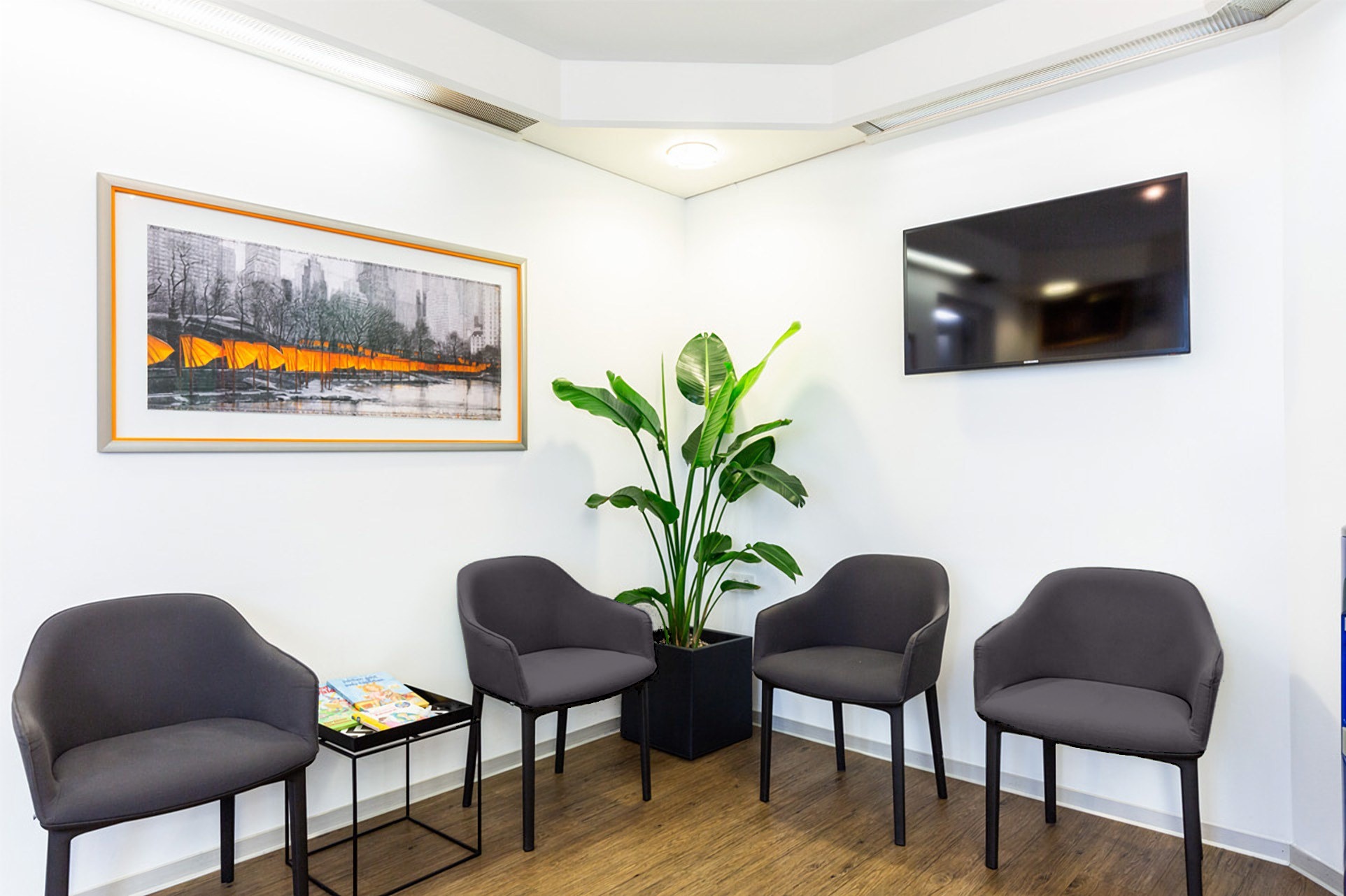 Wartezimmer mit vier grauen Sesseln, Pflanze, Fernseher und Bild mit orangefarbenen Akzenten